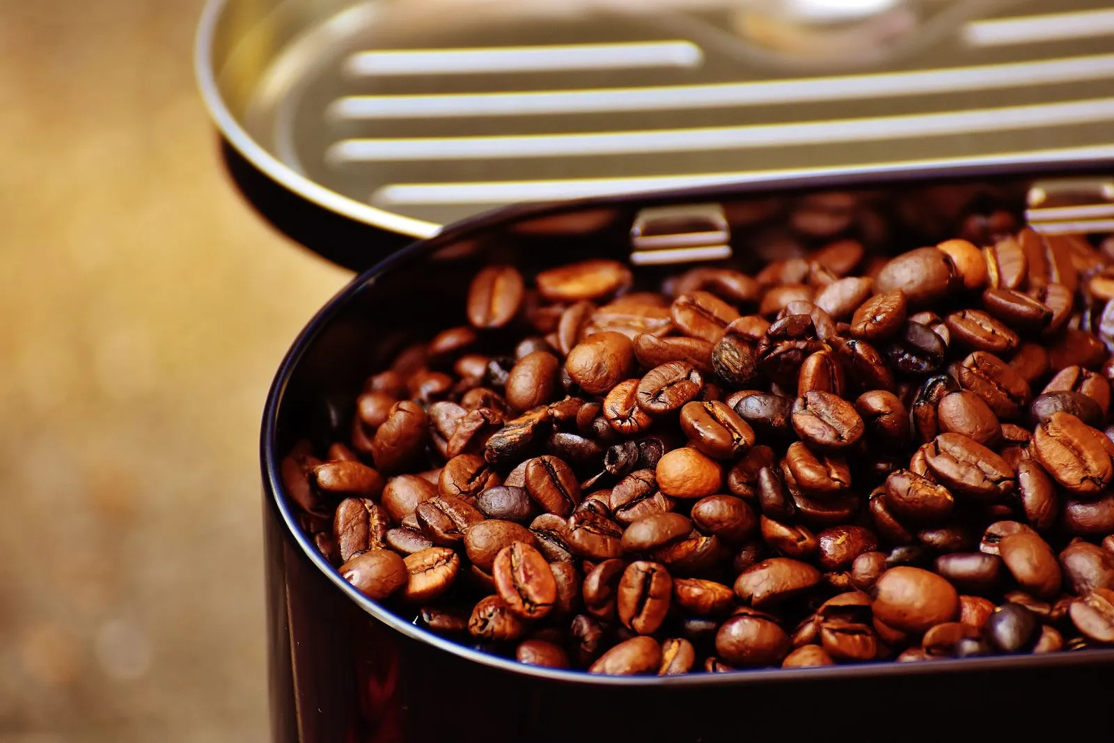 Close-up of roasted coffee beans in an open metal container, highlighting texture.
